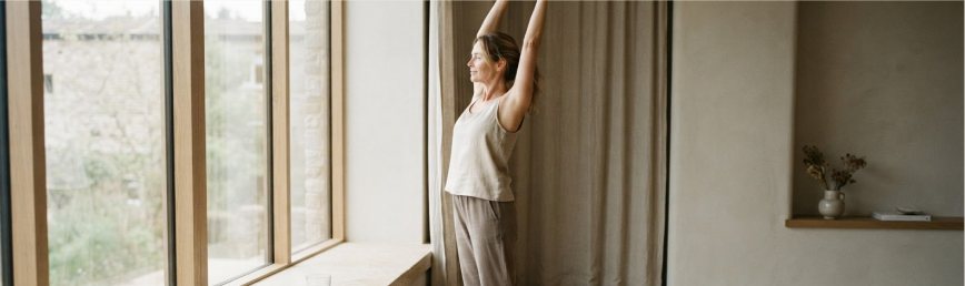 A person stretching by a tall window in soft daylight.